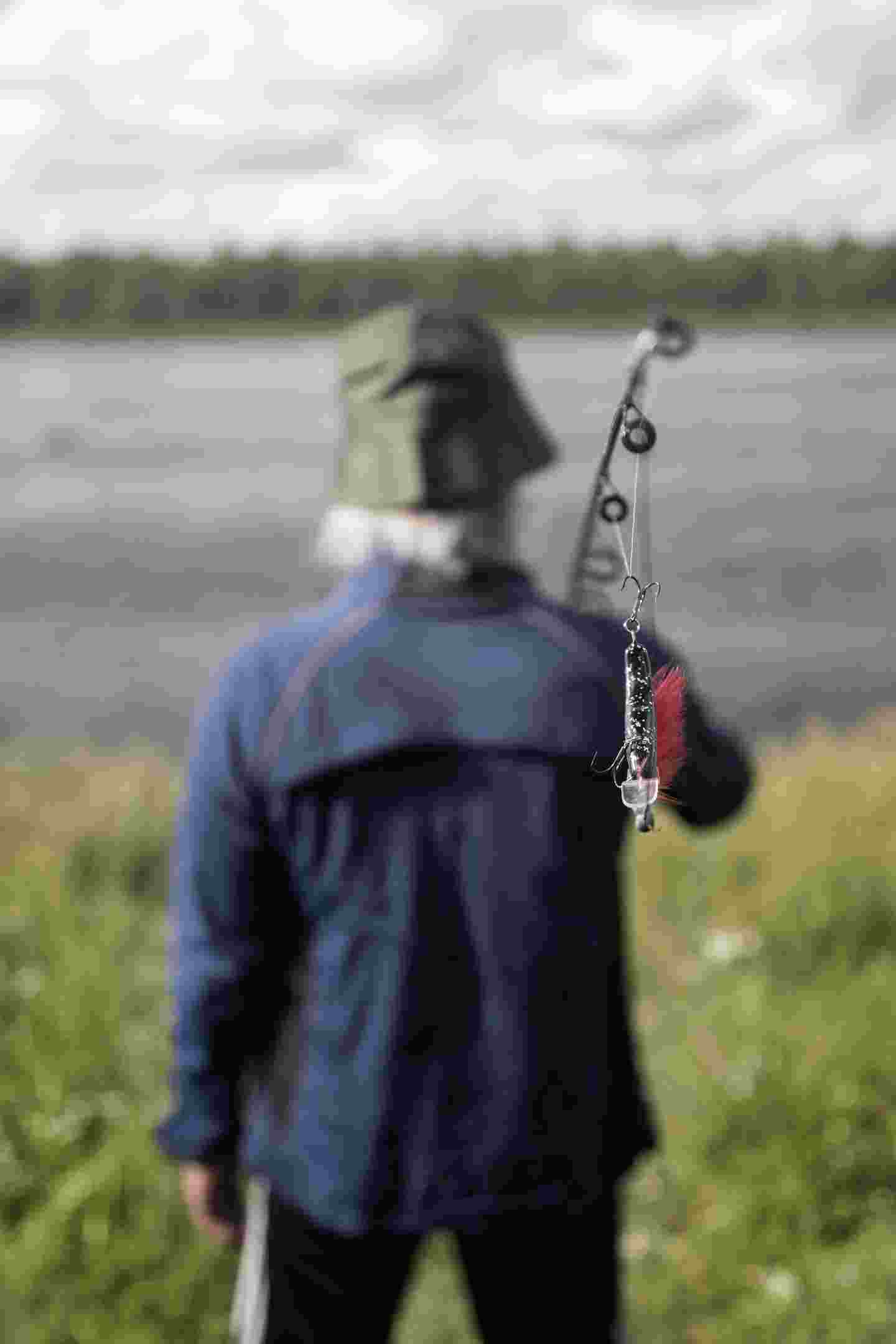 A person standing by a river and holding a fishing rod in his hand.
