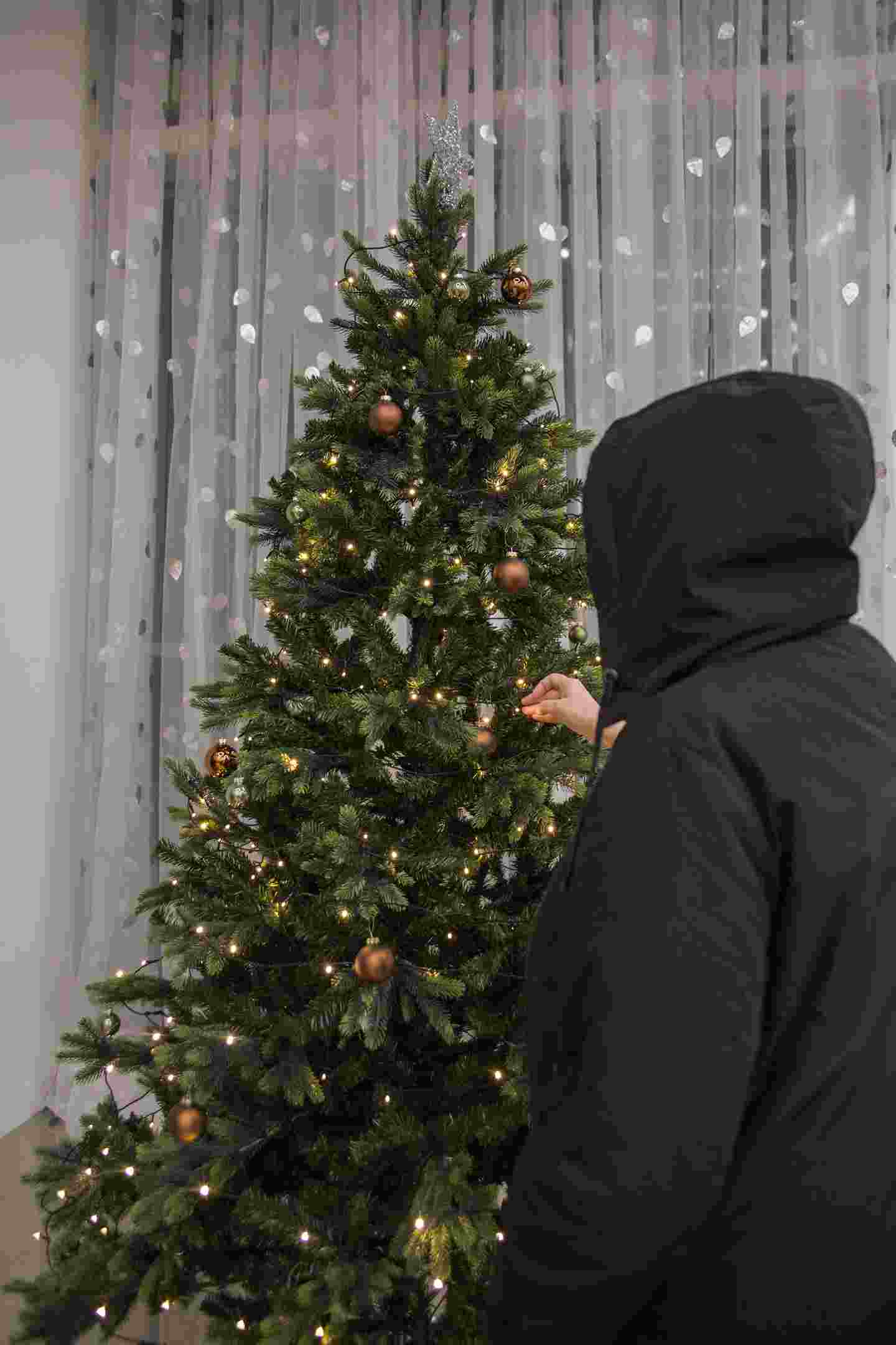 A person placing Christmas lights on a Christmas tree.