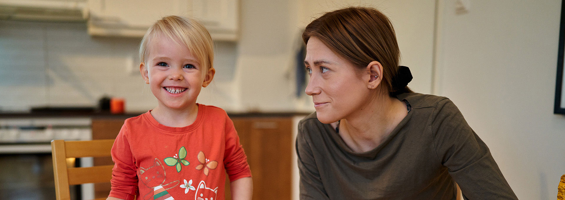 A smiling girl with her hand on her little brother’s shoulder in a room decorated for Christmas.