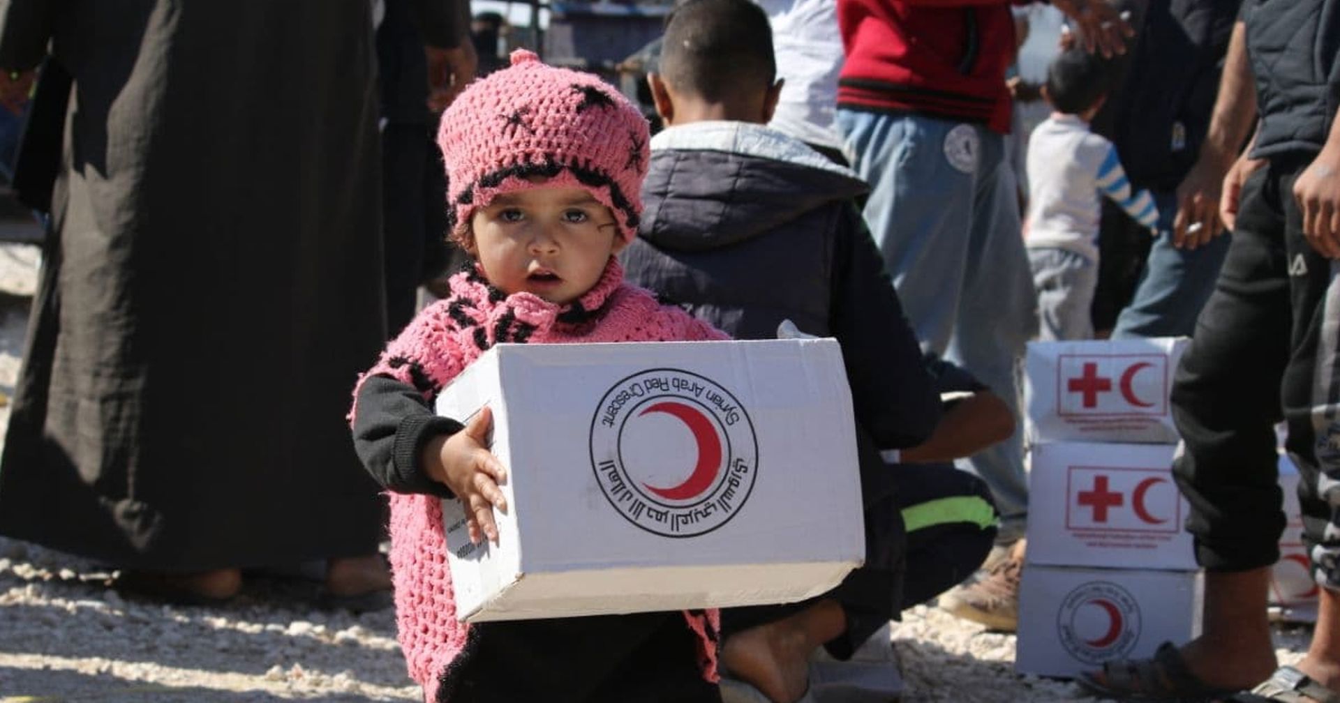 A small Syrian child holding a Red Cross aid package