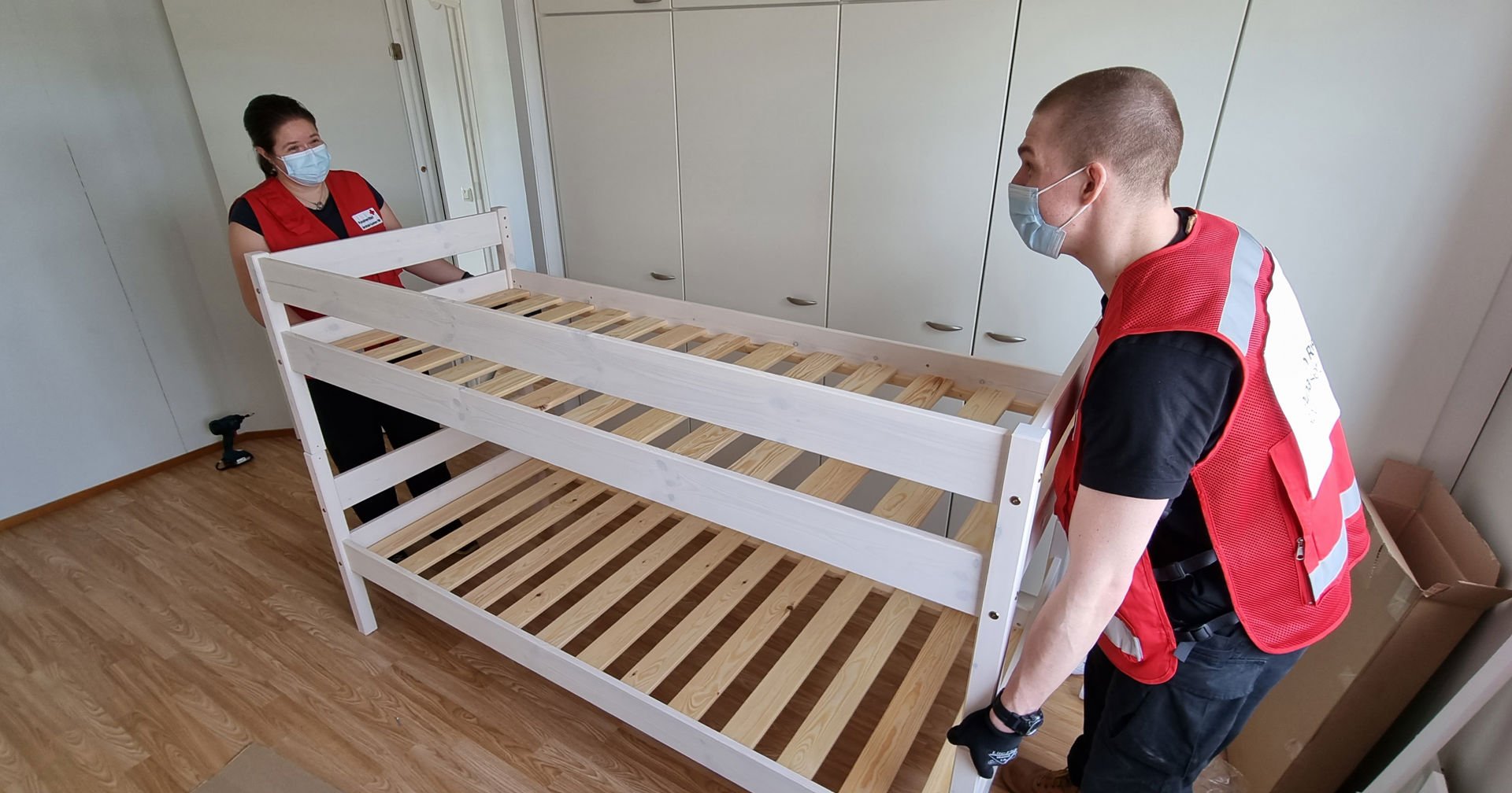 Two volunteers wearing Red Cross clothing carrying a bunk bed.