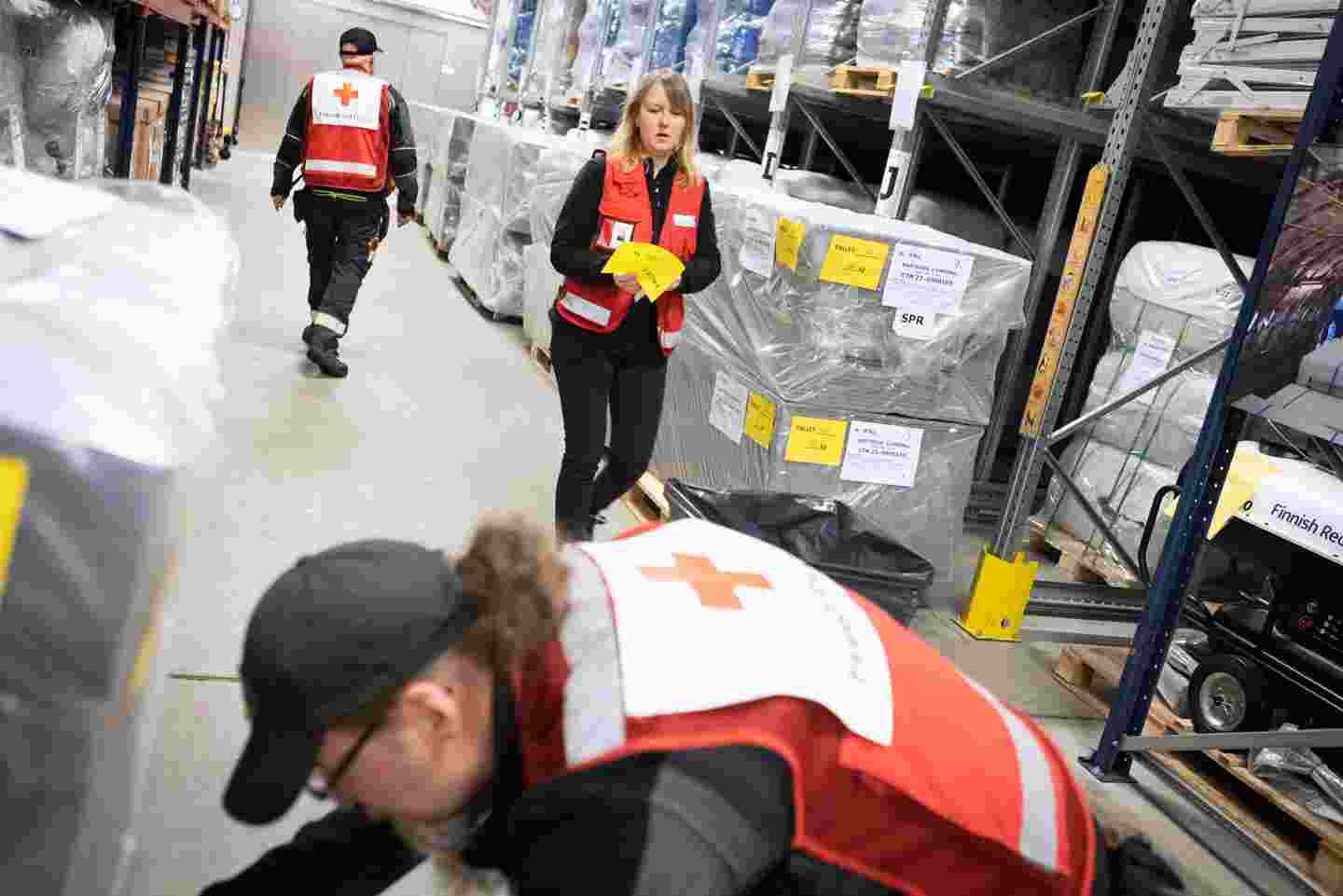Three people working in a storage facility between shelves filled with aid supplies.
