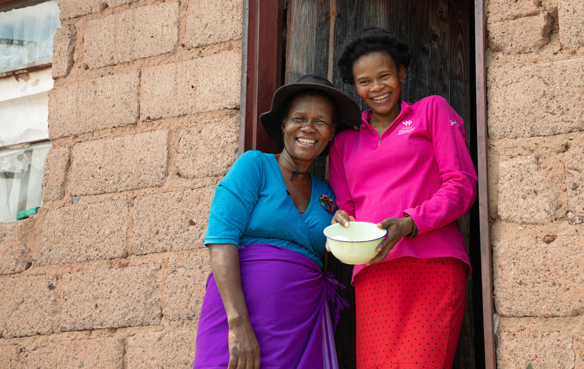 Two people smiling in front of their home in Eswatini.