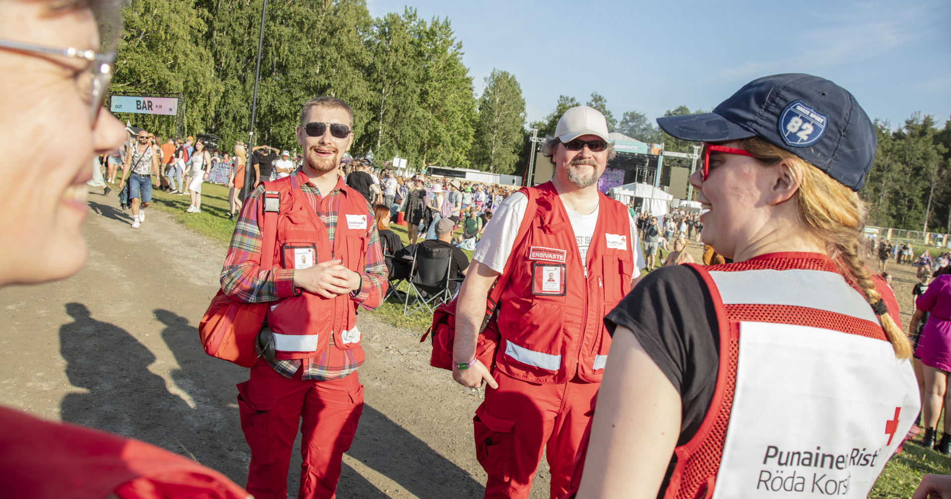 Four smiling Red Cross on-duty volunteers in a sunny festival area.