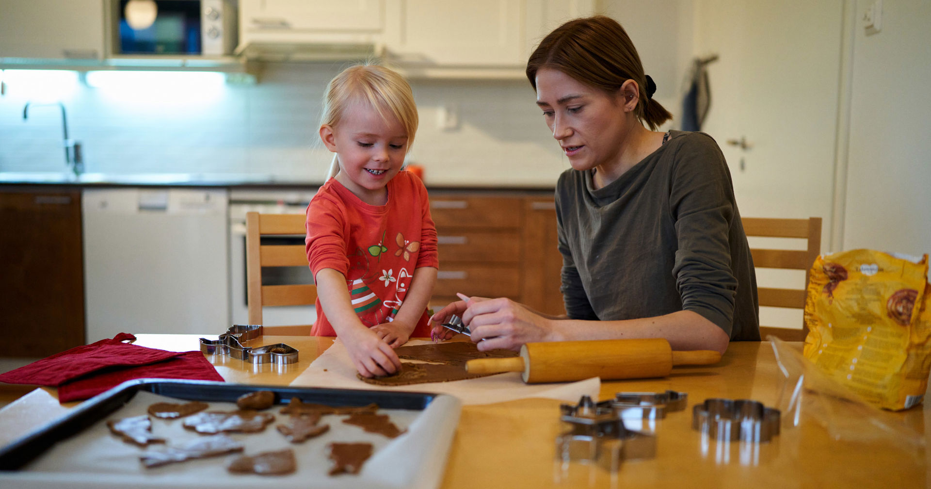 Mother and child baking gingerbread cookies in their home kitchen.