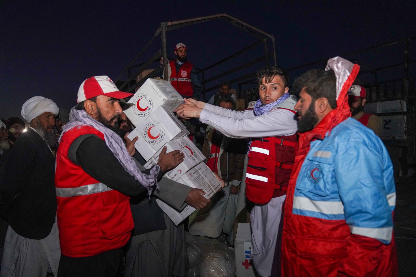 Three volunteers wearing Red Crescent vests lifting boxes with the Red Crescent symbol on them.