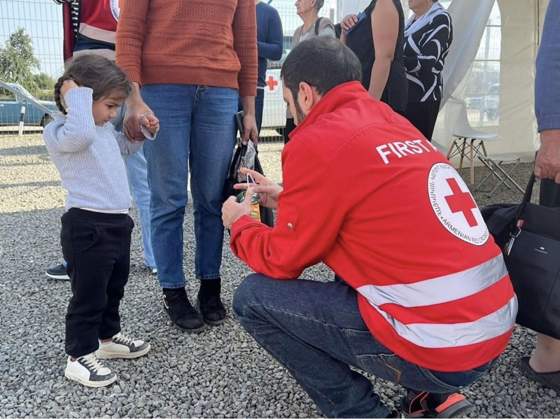 A volunteer wearing an Armenian Red Cross jacket helps a child.