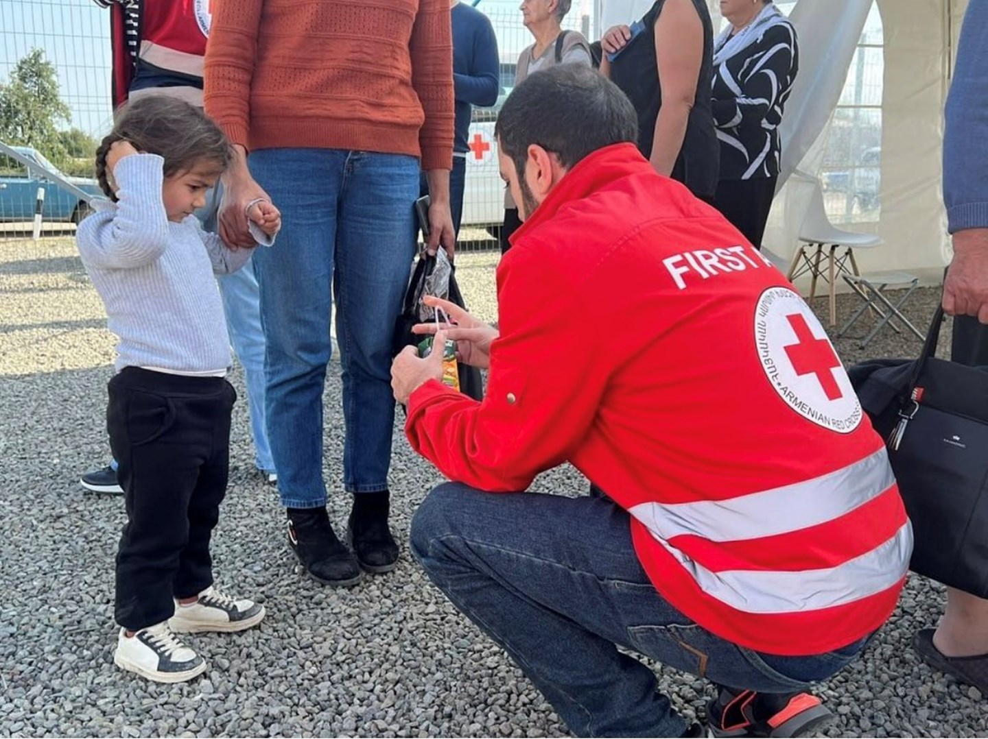 A volunteer wearing an Armenian Red Cross jacket helps a child.