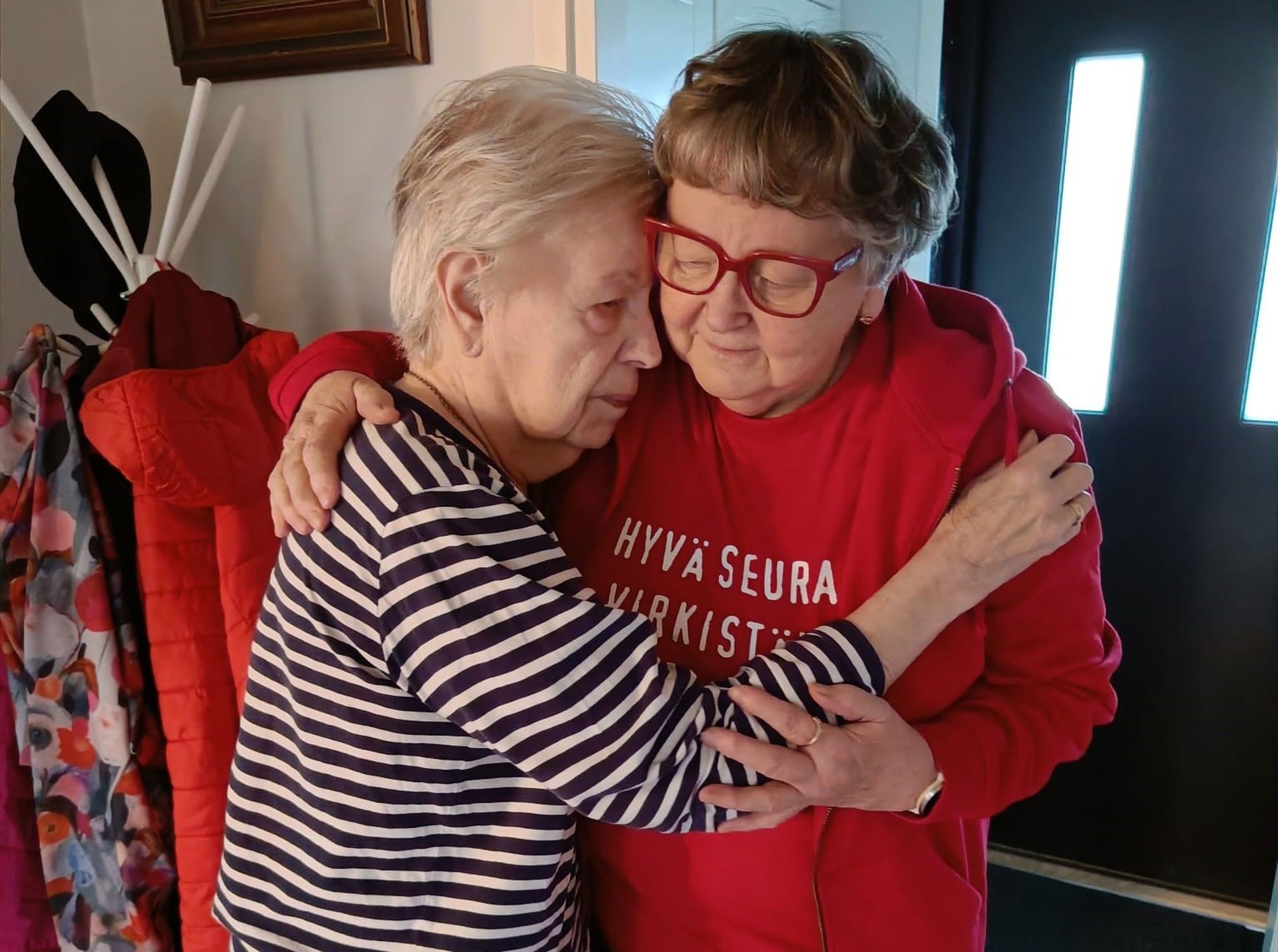 A person in a Red Cross vest is hugging an elderly person.