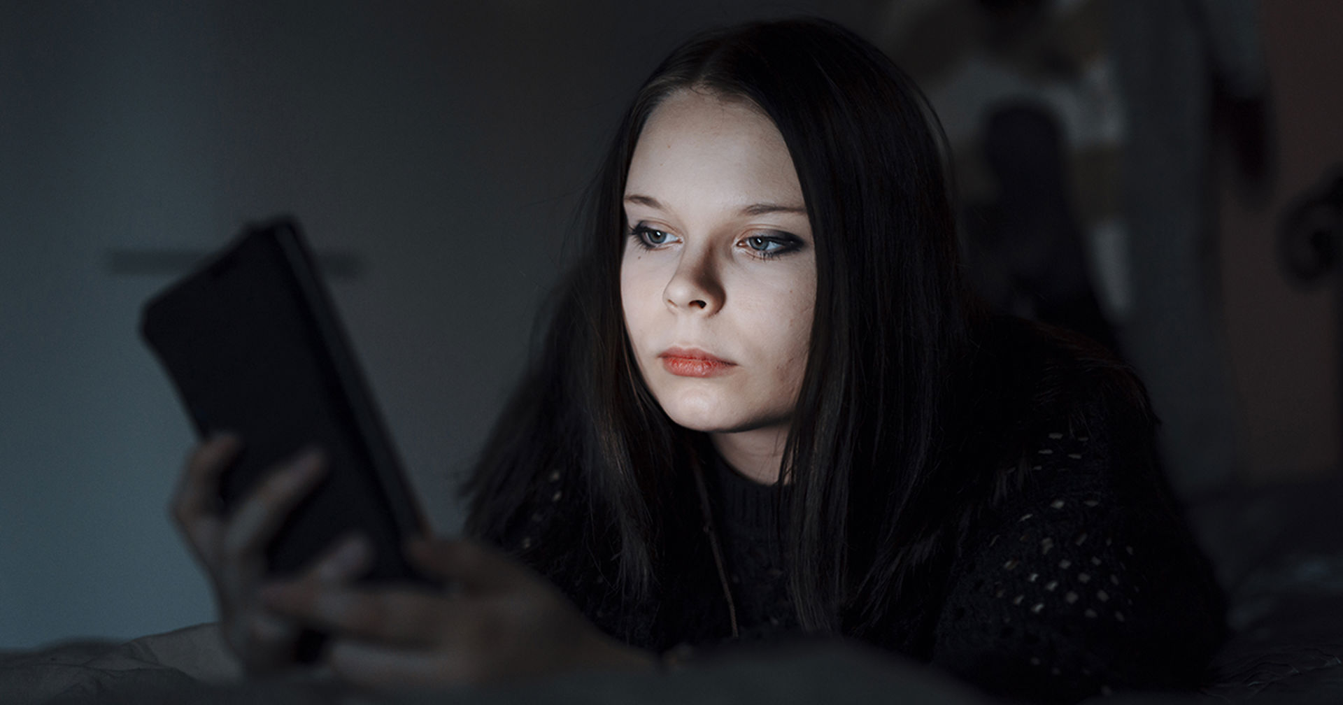 A youngster watches a phone in a dark room.