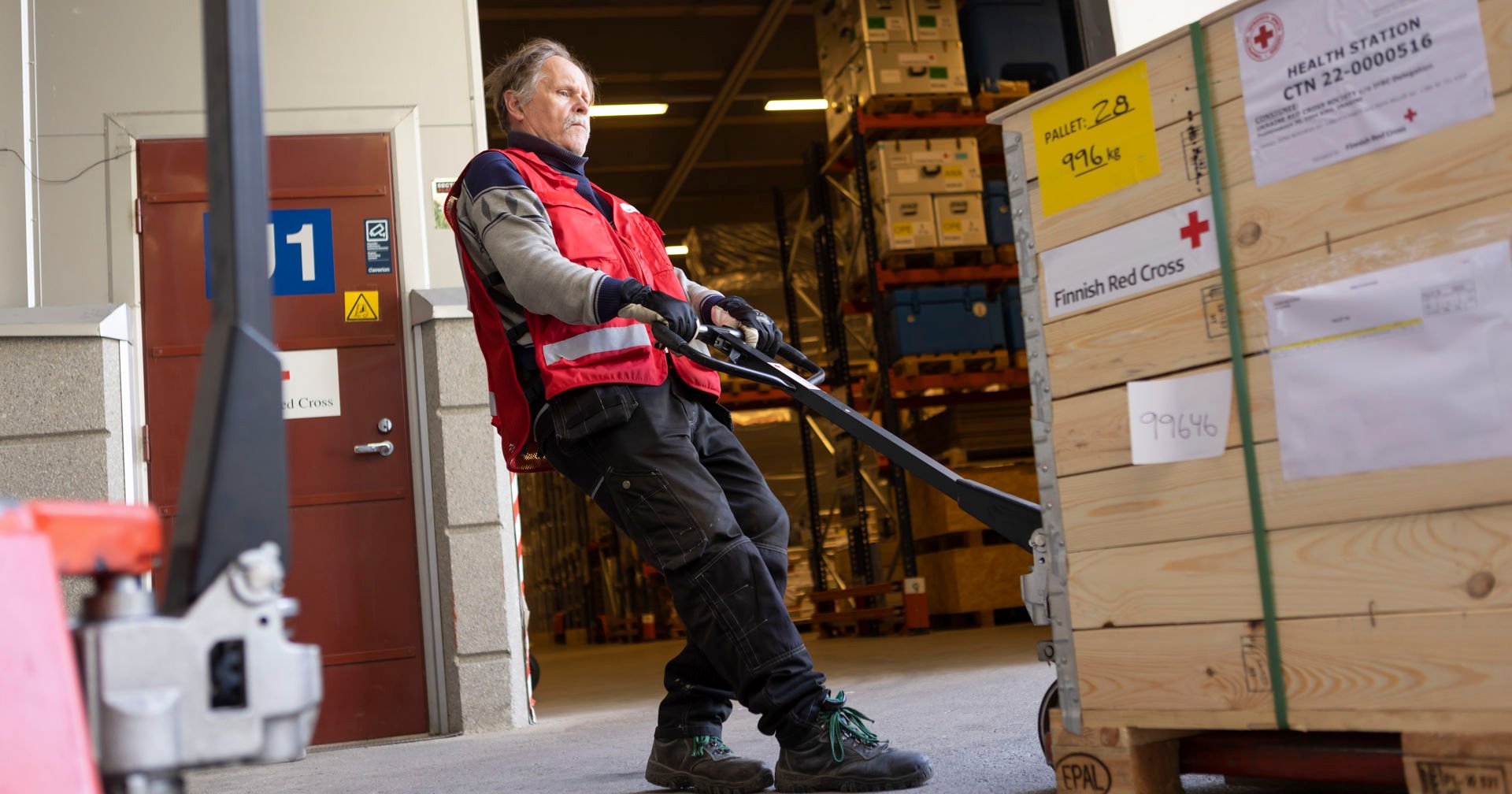 Red Cross employee moving a load with a pallet jack. The boxes read "Health station".