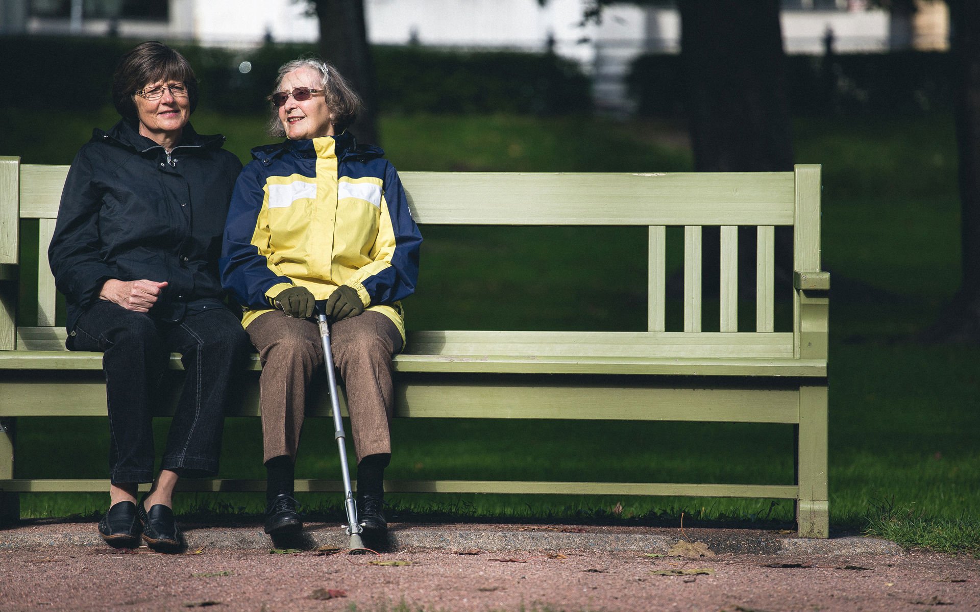 Two elderly women sitting side by side on a park bench.