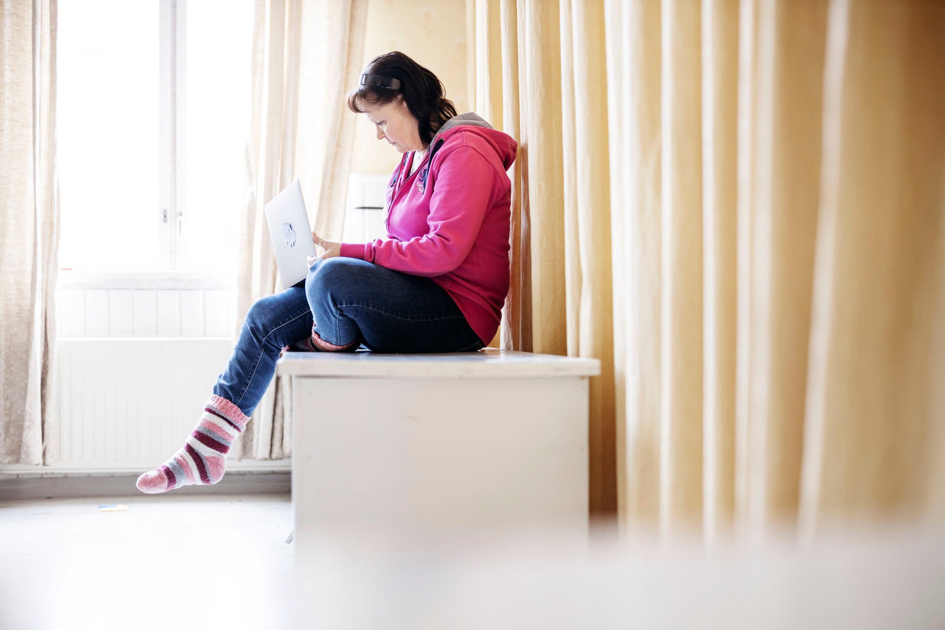 An online volunteer sits in front of a window with a laptop on their lap, typing.