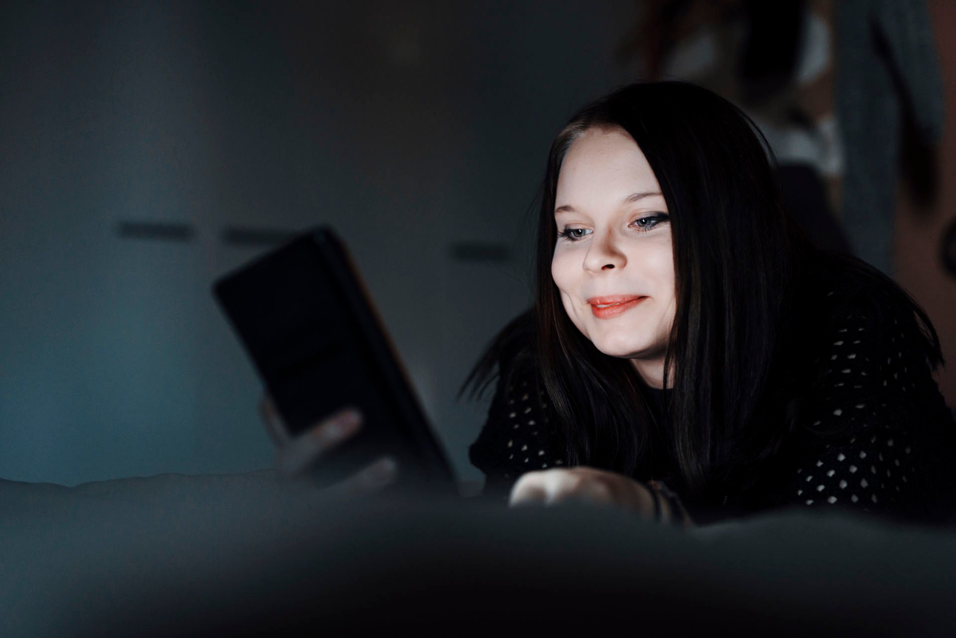 A Red Cross online volunteer is smiling while looking at their phone. The light from the phone's screen illuminates their face