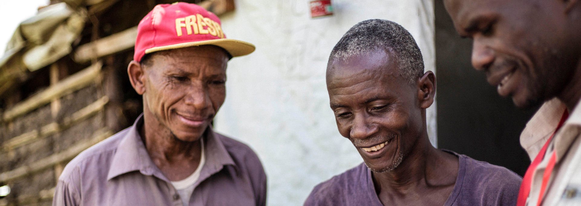 Three smiling African men studying a document with information about a missing family member.