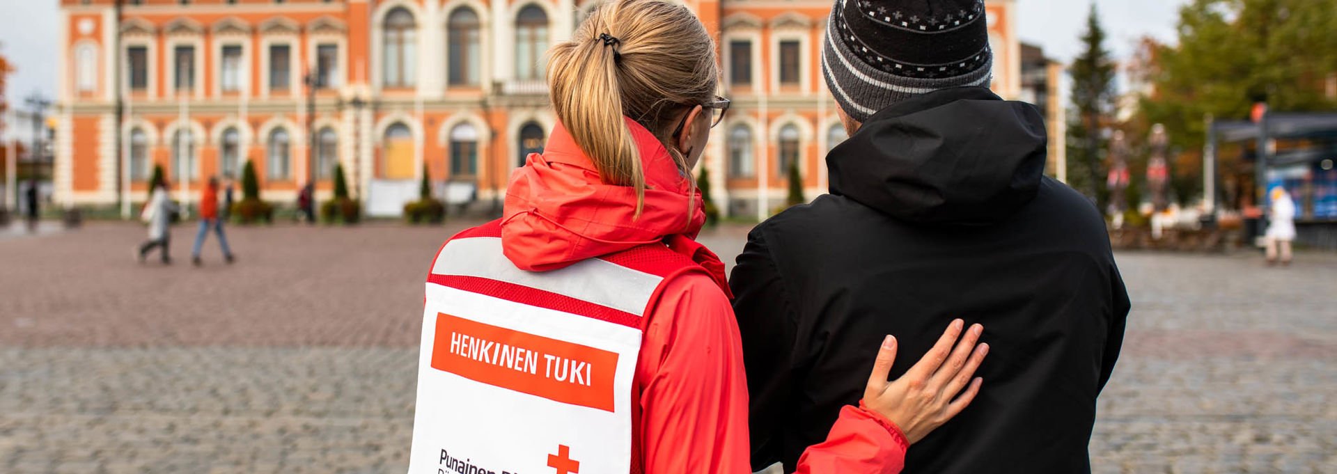 A woman wearing a Red Cross volunteer vest and talking to a shaken man in the Kuopio Market Square.