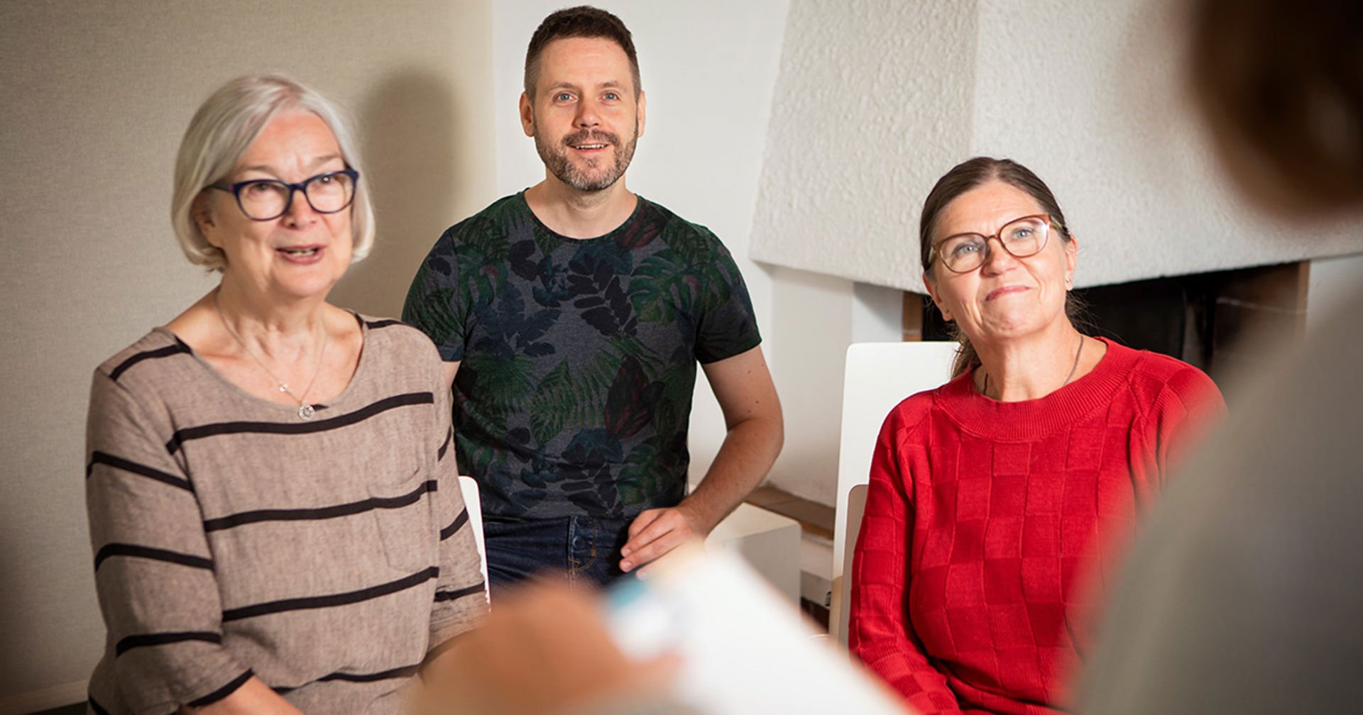 Two women and one man smiling and looking at a fourth person standing opposite them holding a notepad.