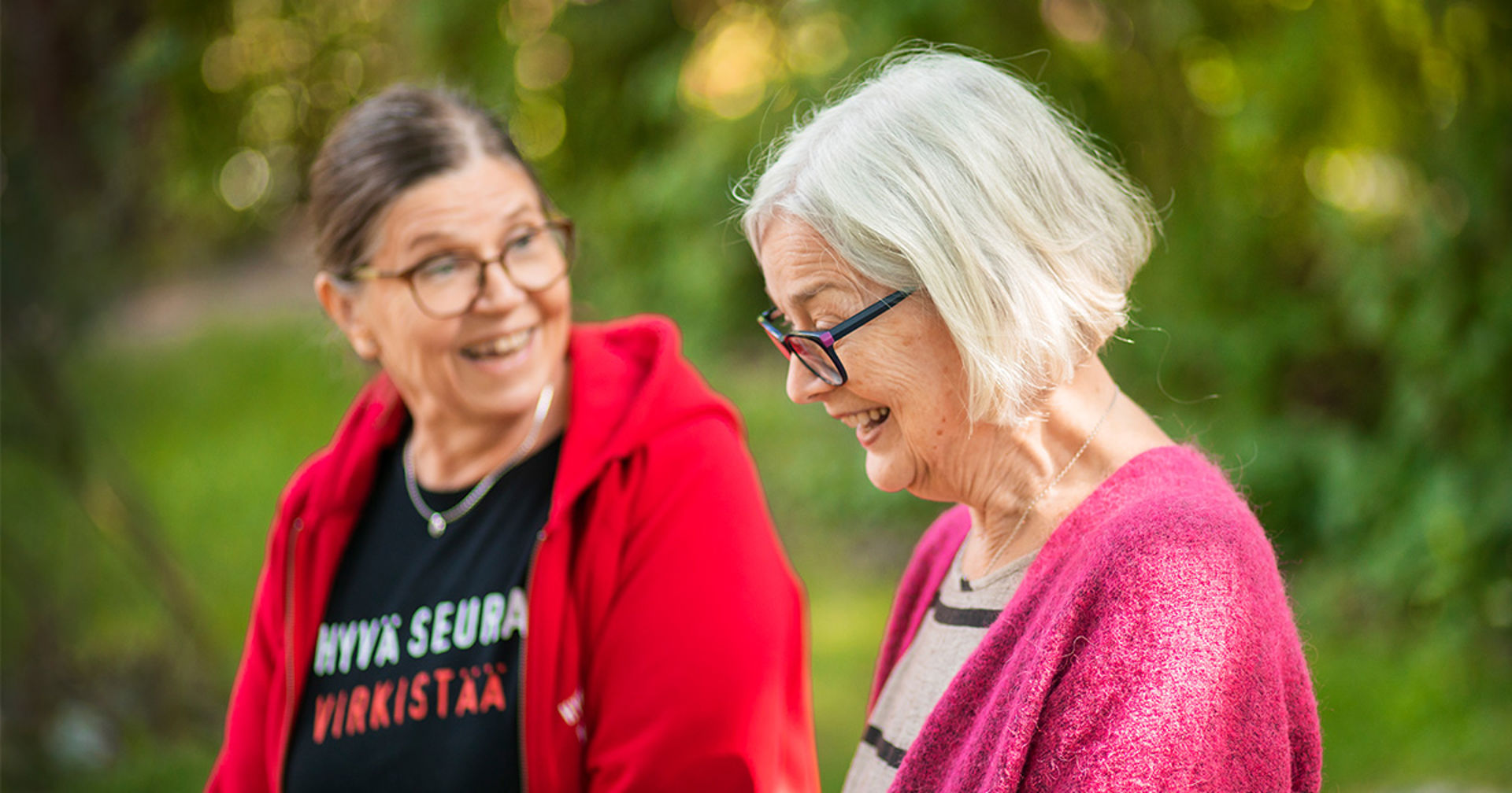 Two smiling women discussing with each other in a green landscape.