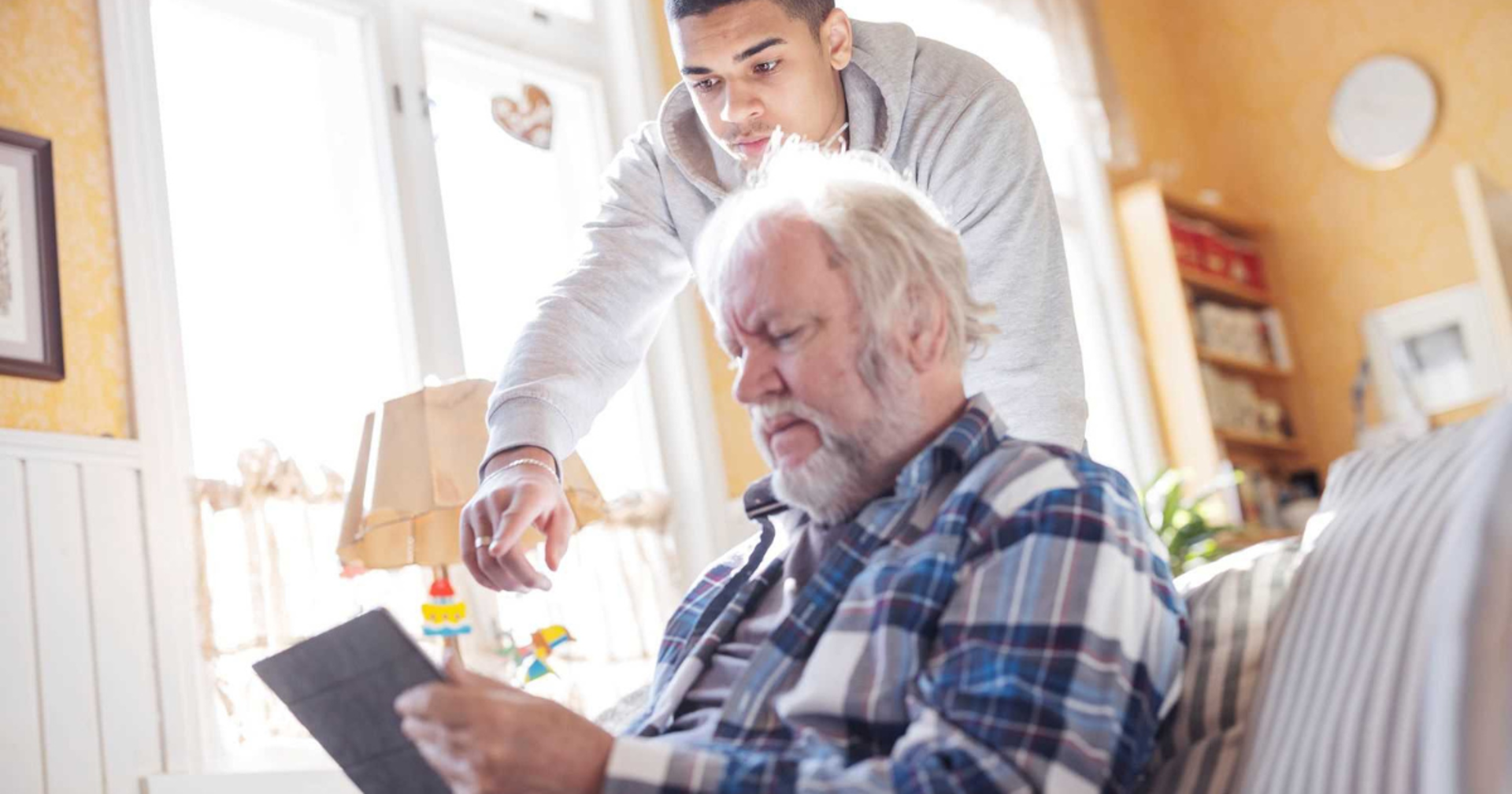 Two people, with the younger one guiding the older person in using a tablet.