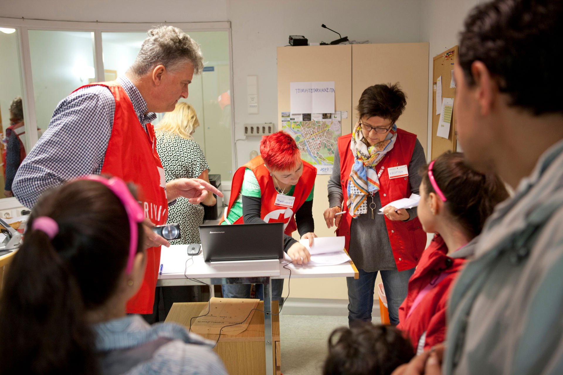 Several people in Red Cross clothing record arriving asylum seekers.