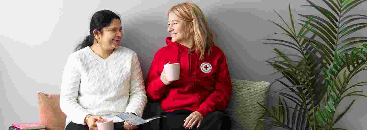 Two people smiling and sitting on a sofa holding a Red Cross brochure and a cup of coffee.