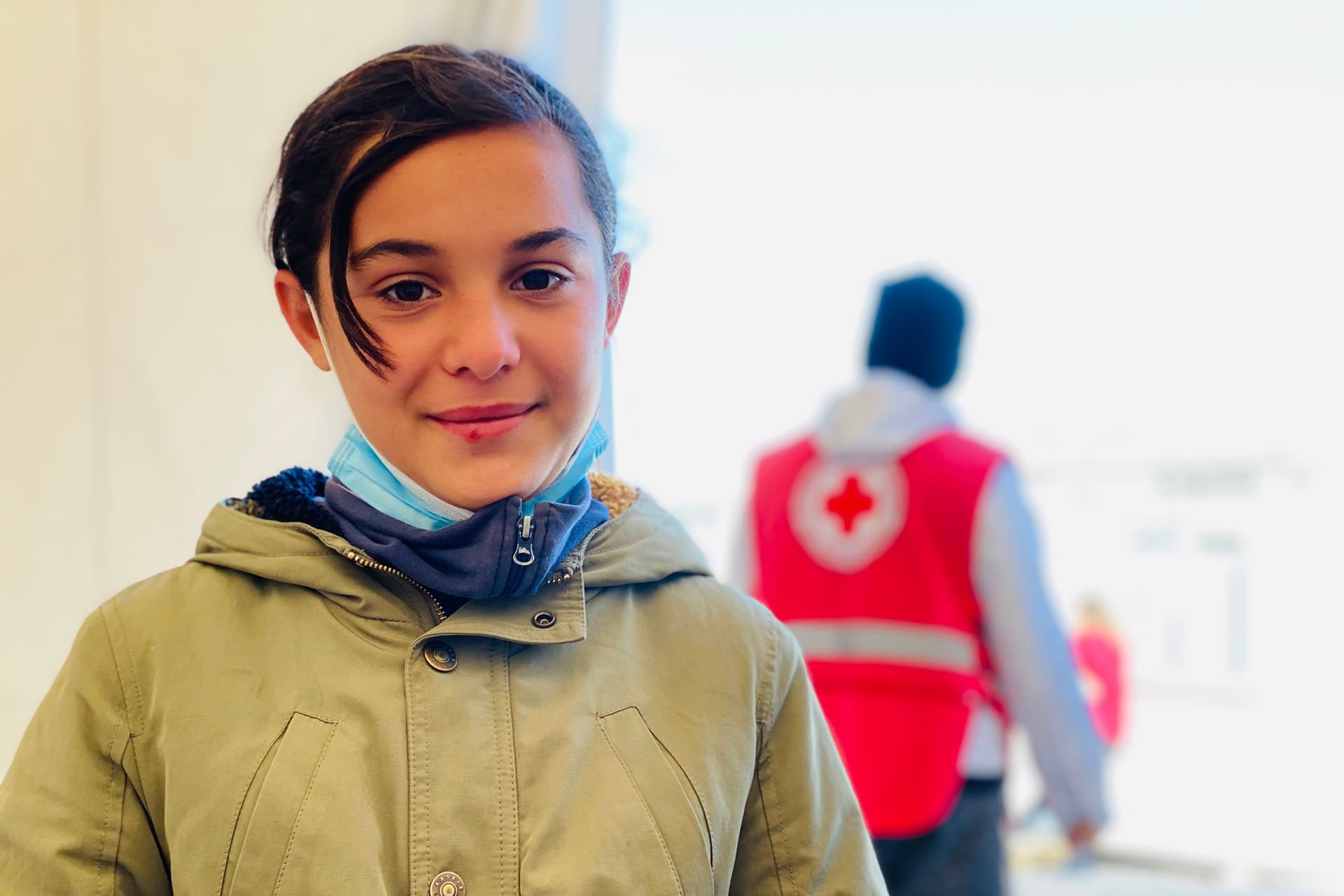 Rokia stands smiling towards the camera, with a Red Cross worker in uniform in the background.