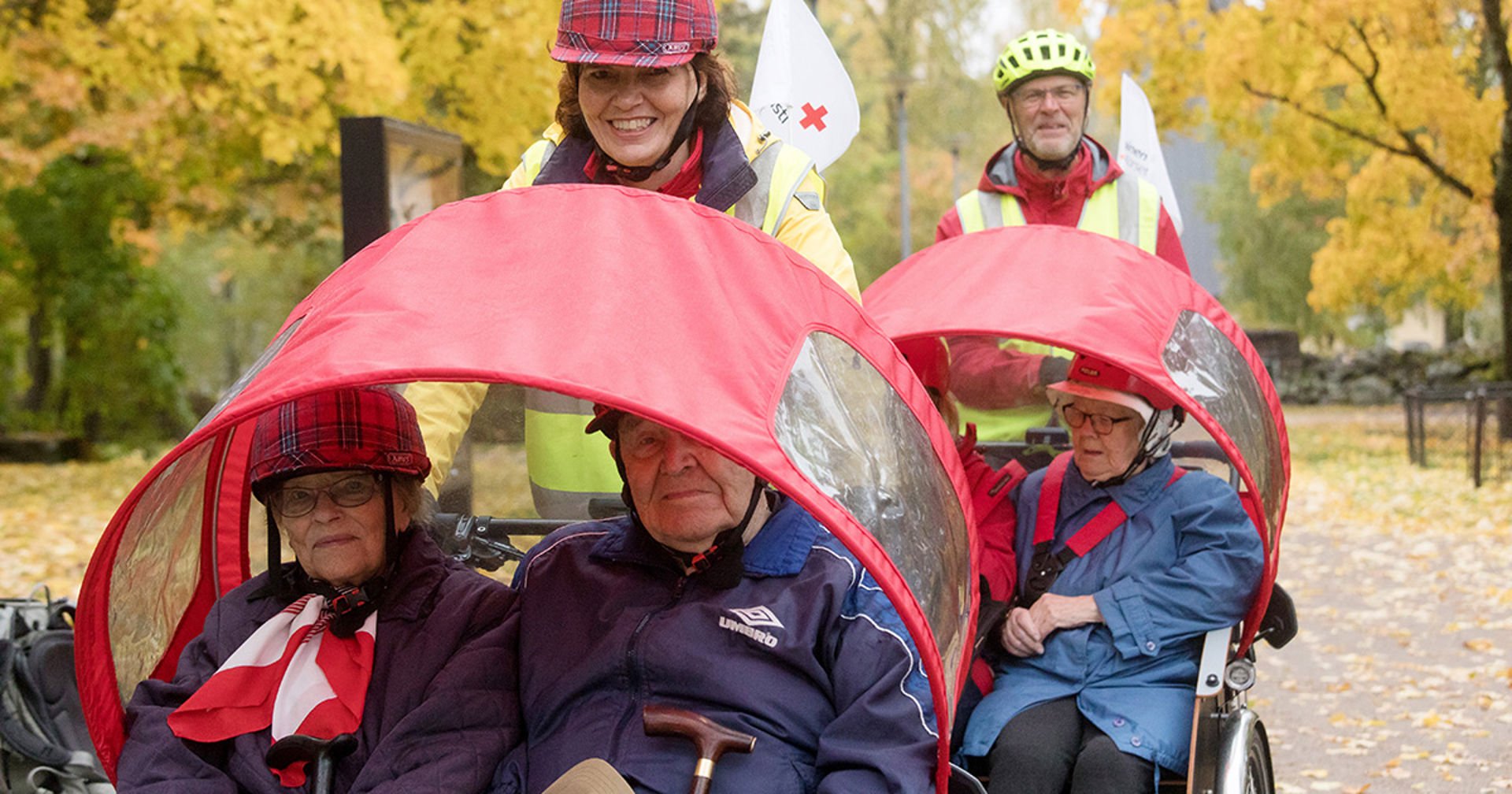 Two Red Cross volunteers taking senior citizens outdoors on rickshaws.