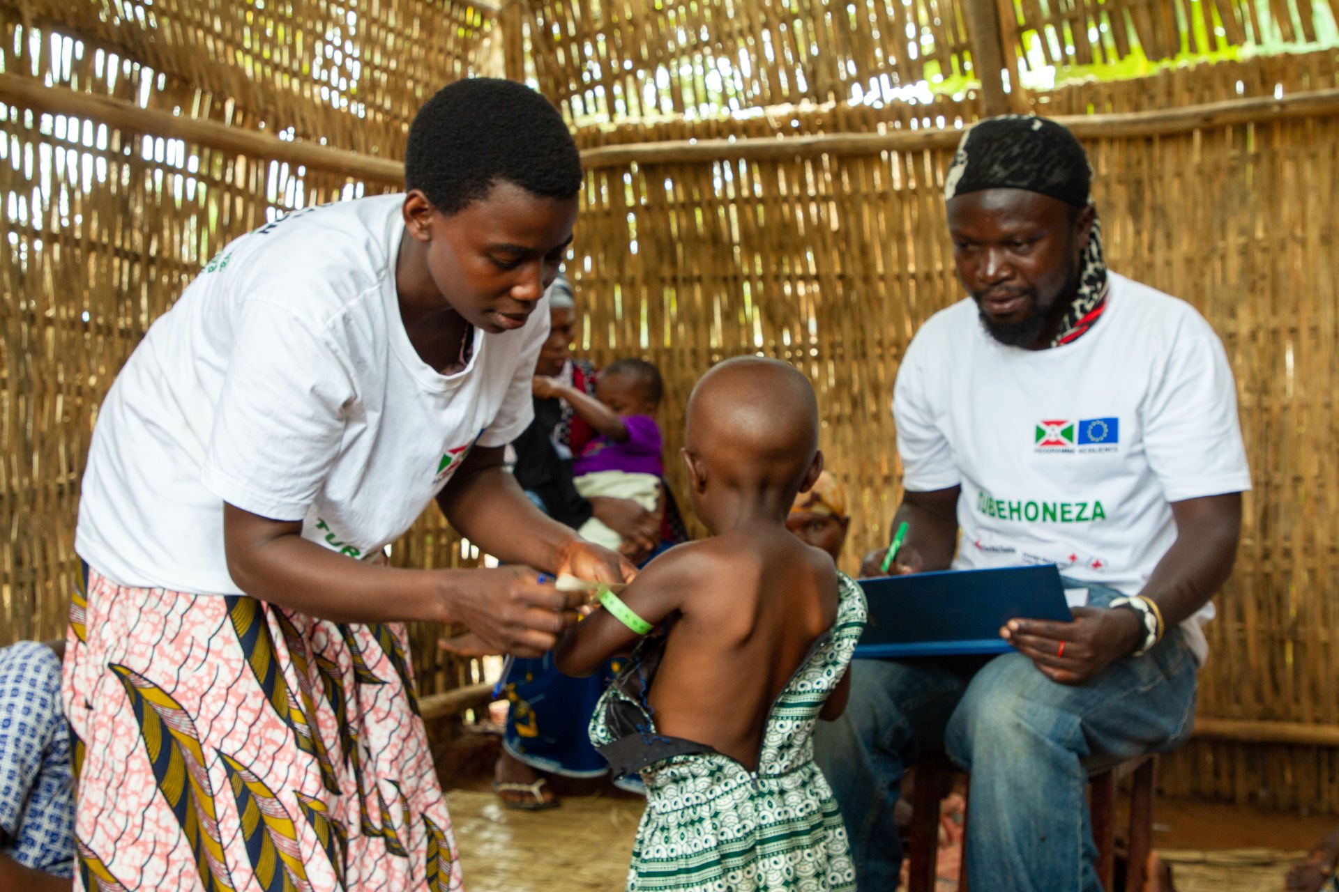 A woman measuring the circumference of a child’s arm, a man making notes.