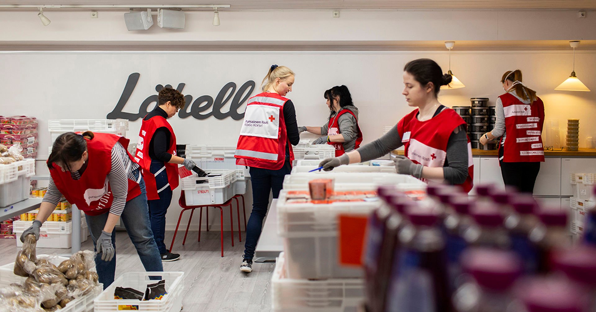 Six people in Red Cross volunteer vests arranging food packages.