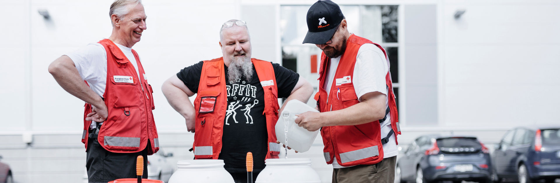 Three smiling people in Red Cross clothes filling clean water containers.