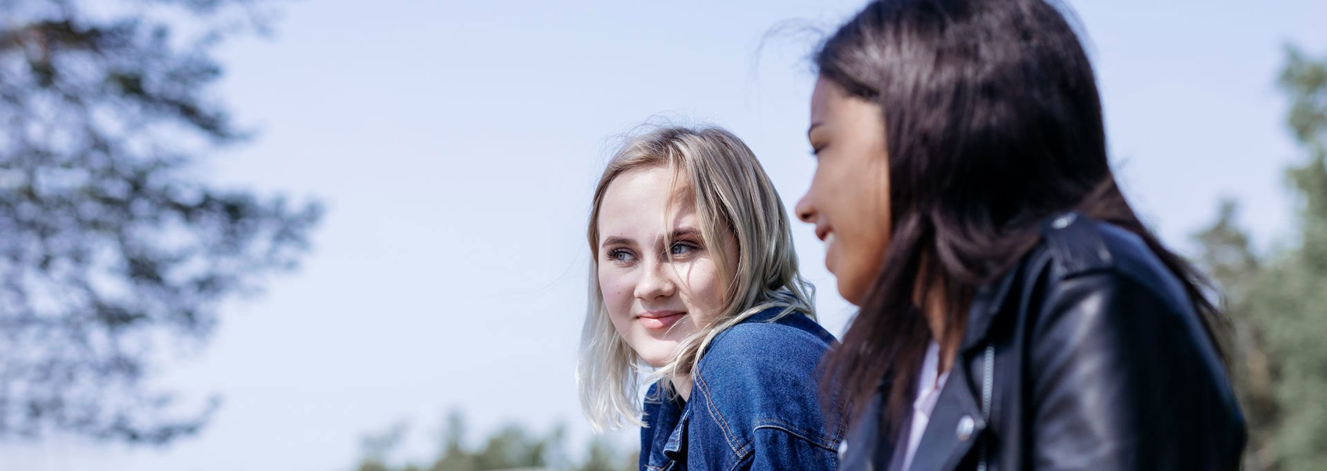 Two smiling young women talking outside in the sun.