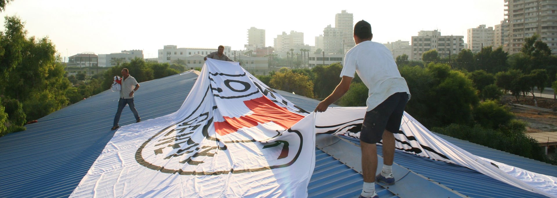 Three men positioning the protection symbol of the red cross to a roof in the sunlight.