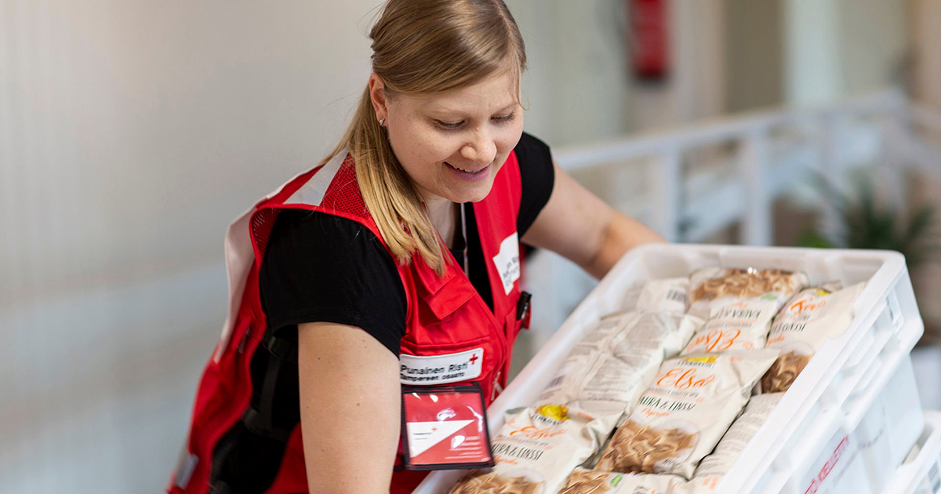 A person in Red Cross clothing is holding a large bread box.