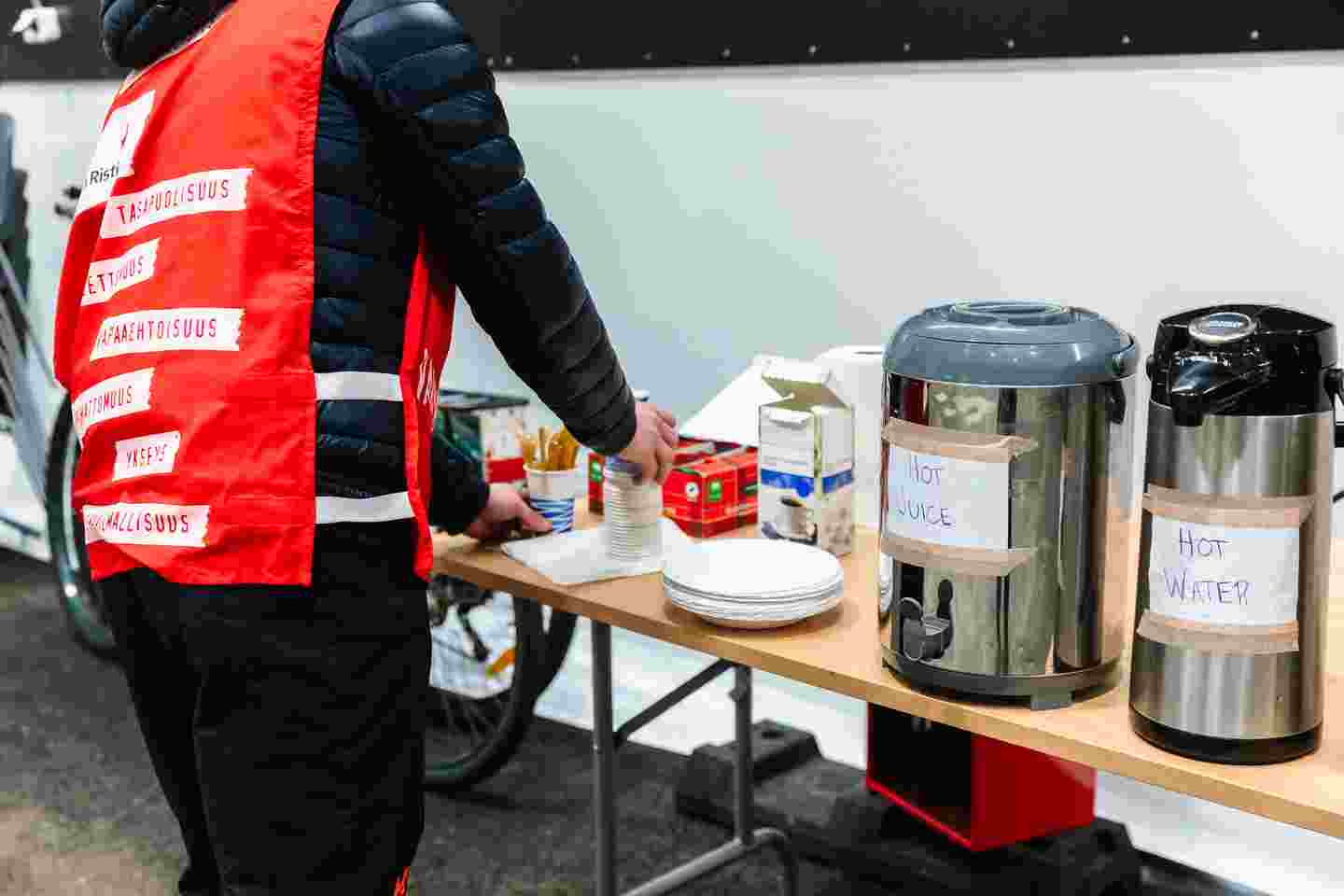 A Red Cross volunteer is organising a table with thermoses filled with hot beverages.