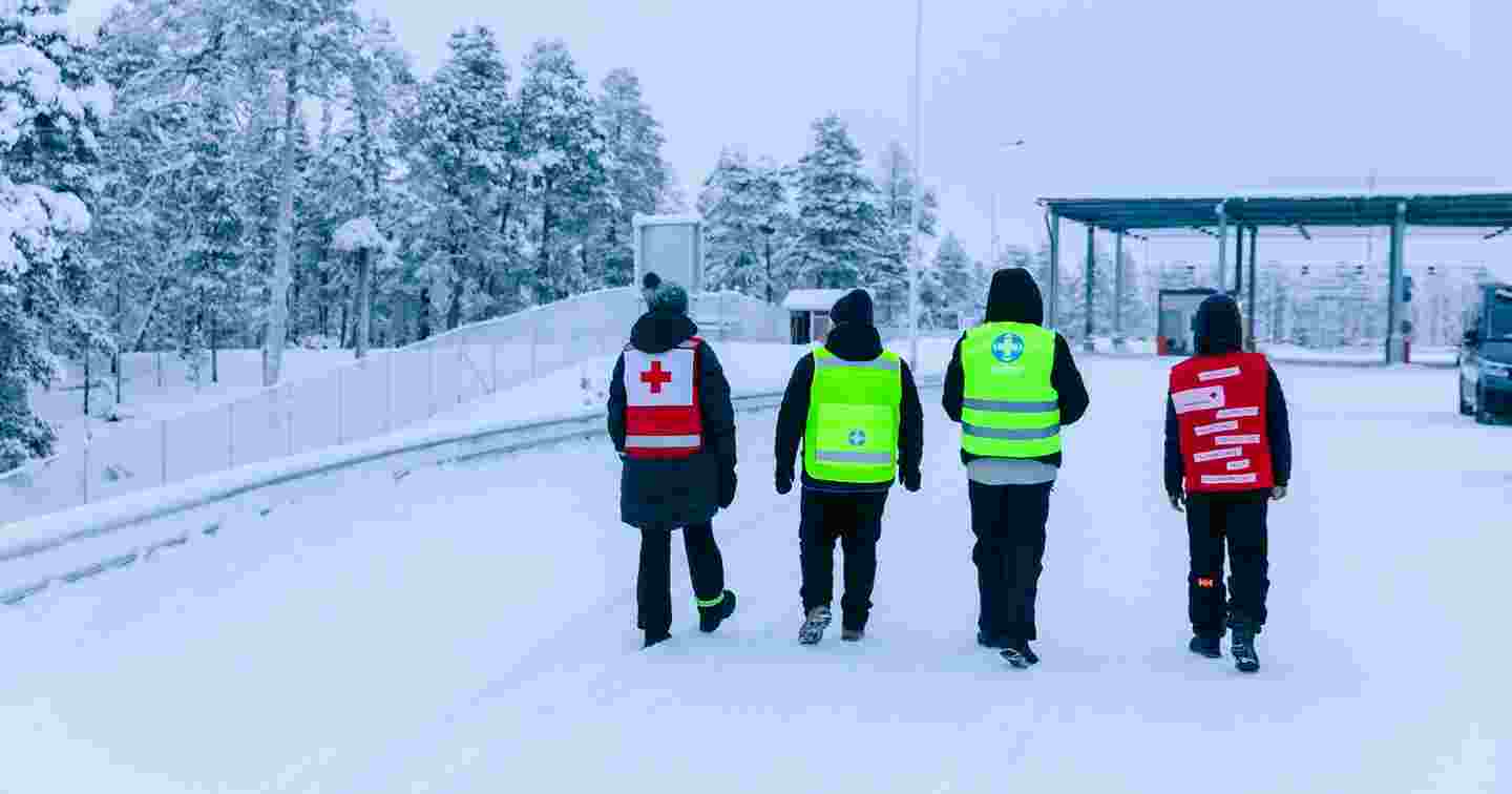Two Red Cross volunteers and two Voluntary Rescue Service volunteers walking towards the border area in winter conditions.