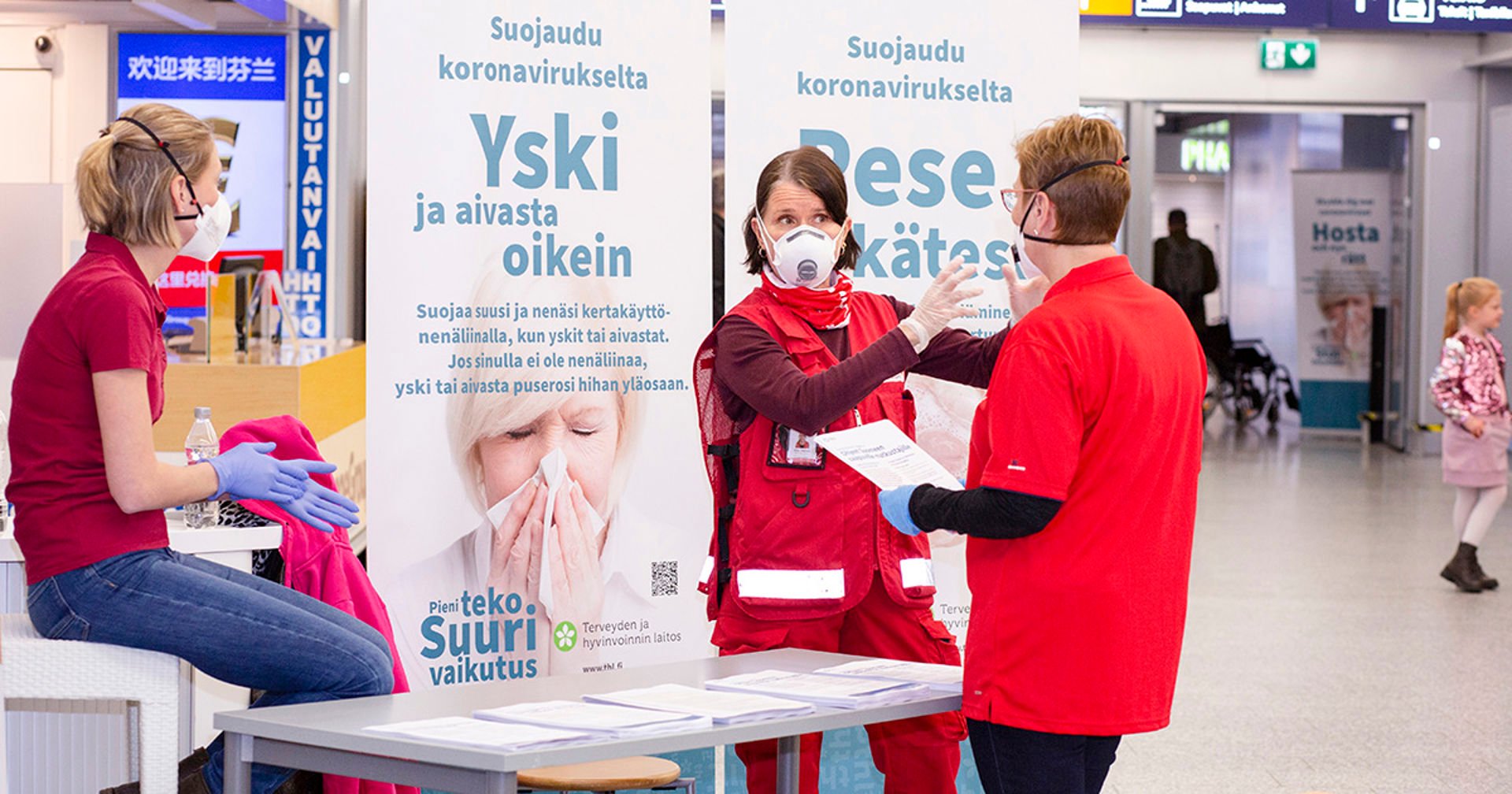 Three people wearing Red Cross vests at the coronavirus information desk at Helsinki Airport.